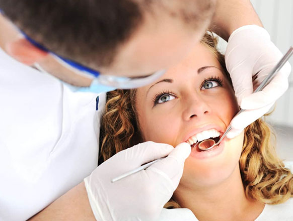 Male dentist examining a female patients teeth.  He is us is using a dental mirror